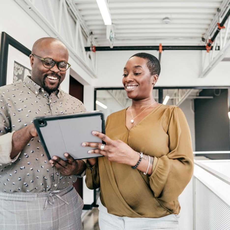 Two black people smiling and looking at tablet in office.